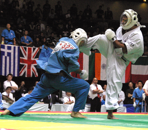 Combate de Kudo en un Campeonato Mundial: dos competidores con casco protector frente a las banderas de los países participantes